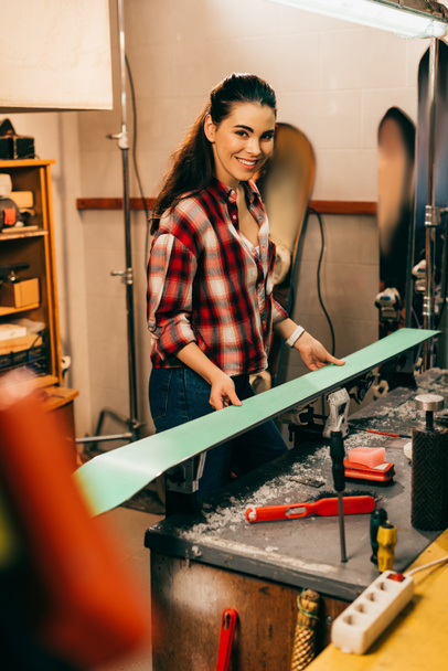 smiling worker holding ski and looking at camera in repair shop  - Photo, Image