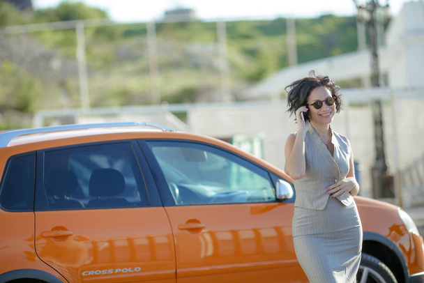 Mulher de negócios em um terno leve elegante falando em um telefone celular em um parque de estacionamento
 - Foto, Imagem