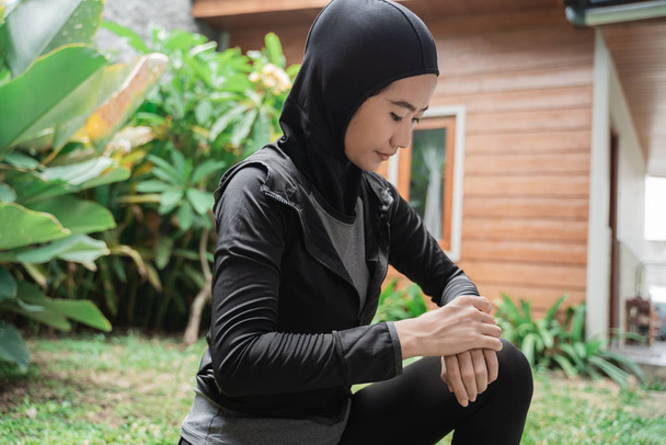 Türbanlı sporcu Asyalı kadın, saati ayarlamak için akıllı bir bilekliğe bakıyor. - Fotoğraf, Görsel