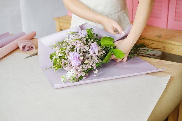kobieta kwiaciarnia podejmowania bukiet fioletowe kwiaty wewnątrz. Kobieta kwiaciarnia przygotowuje bukiet w kwiaciarni. przedsiębiorczość, małe przedsiębiorstwa, koncepcja miejsca pracy. Przestrzeń kopiowania - Zdjęcie, obraz