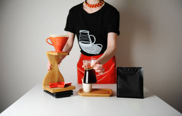 Menina barista na moda serve café filtro. Estação de gotejamento de madeira. Saia de couro vermelho, t-shirt preta. Lugar para design
 - Foto, Imagem
