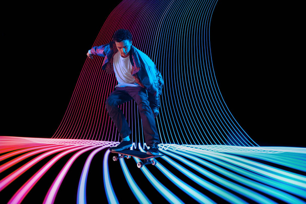 Caucasian young skateboarder riding on dark neon lighted line background - Fotoğraf, Görsel