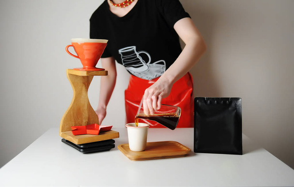 Trendy barista girl serves filter coffee. Wood drip station. Red patent leather skirt, black t-shirt. Place for design - Photo, Image