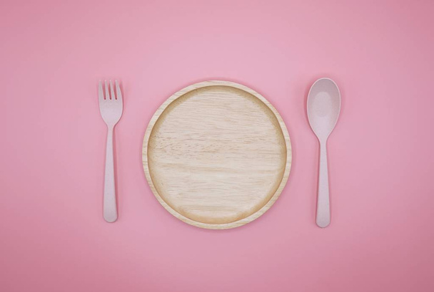 růžová vidlička, lžíce a dřevěný talíř na růžovém pozadí - Fotografie, Obrázek