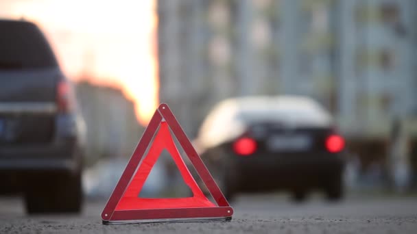 Piros vészleállító tábla a törött homályos autó mögött villogó fényekkel az esti városi járdaszegélyen. - Felvétel, videó