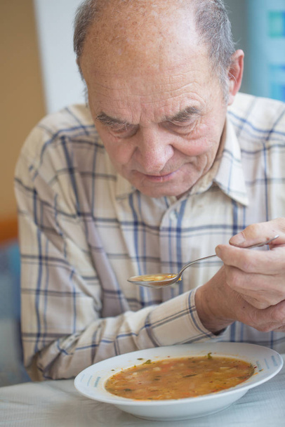 Elderly man with Parkinsons disease holds spoon in both hands - Фото, изображение