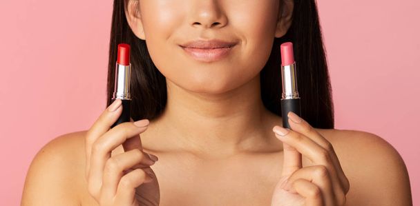 Smiling girl holding two lipsticks, choose between red and pink - Foto, Bild