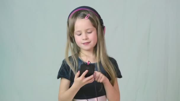 Pretty smiling cild girl listening to music in big pink earphones. - Felvétel, videó