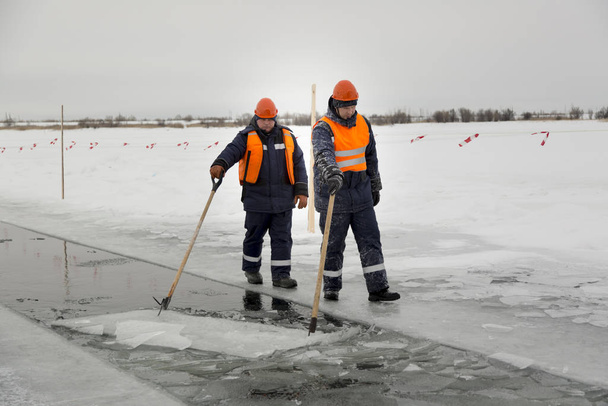 Робітники плавають по льодовикових блоках вздовж каналу, вирізаного замерзлим озером
 - Фото, зображення