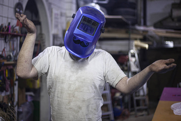 Cheerful welder in a welding mask. Mask mustache for eye protection. Master in his workshop. A man at work in the garage. The welder is getting ready for work. A husband in his realm of handicrafts. - Foto, Bild