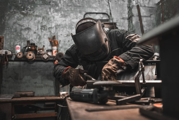 Trabajador en una máscara de soldador trabaja en un taller para soldador. El hombre fabrica productos de hierro. El tipo trabaja con una máquina de soldadura usando una máscara para proteger sus ojos de los peligrosos rayos
 - Foto, imagen