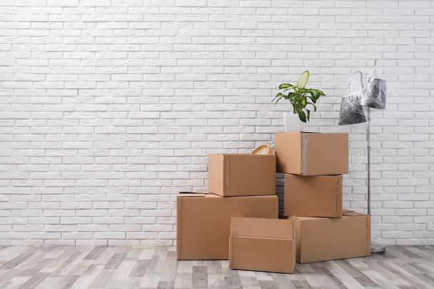Pile of cardboard boxes and houseplant near white brick wall, space for text. Moving day - Fotoğraf, Görsel