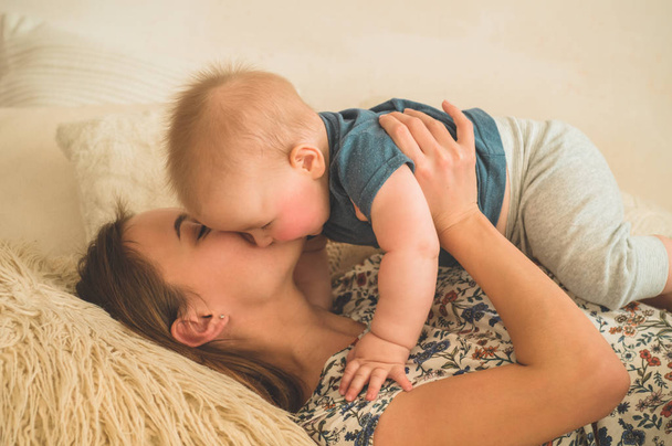 Αγάπη και οικογένεια. Το πορτραίτο ενός μικρού αγοριού με τη μητέρα στο κρεβάτι. Η μαμά παίζει και φιλάει το παιδί της - Φωτογραφία, εικόνα
