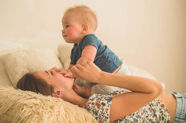 Love and family. Home portrait of a baby boy with mother on the bed. Mom play and kissing her child - Fotografie, Obrázek