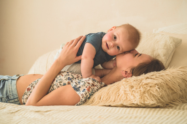愛と家族ベッドの上で母親と赤ちゃんの男の子の家の肖像画。ママプレイとキス彼女の子供 - 写真・画像