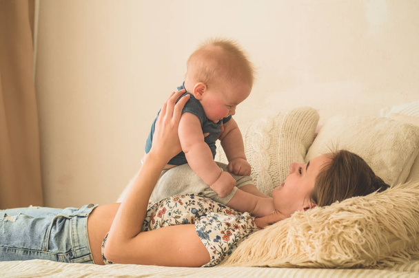 Любов і сім'я. Домашній портрет хлопчика з матір'ю на ліжку. Мама грає і цілує свою дитину
 - Фото, зображення