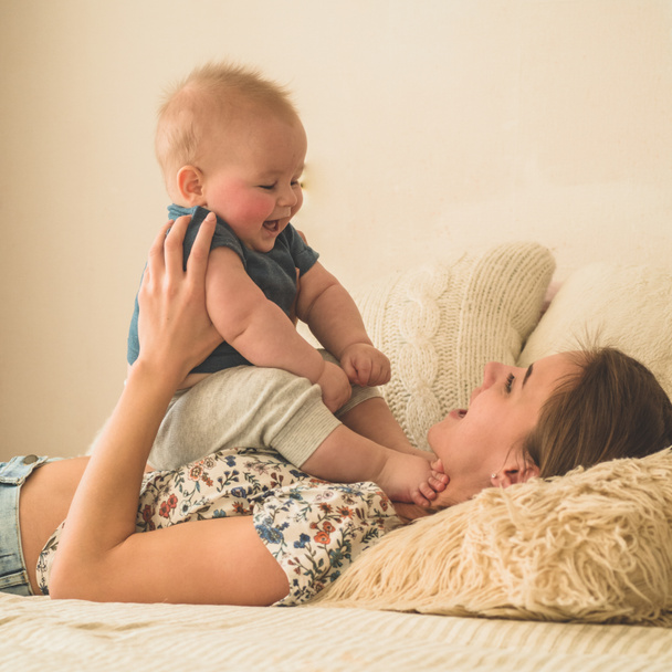 Liefde en familie. Thuisportret van een jongetje met moeder op bed. Moeder spelen en kussen haar kind - Foto, afbeelding