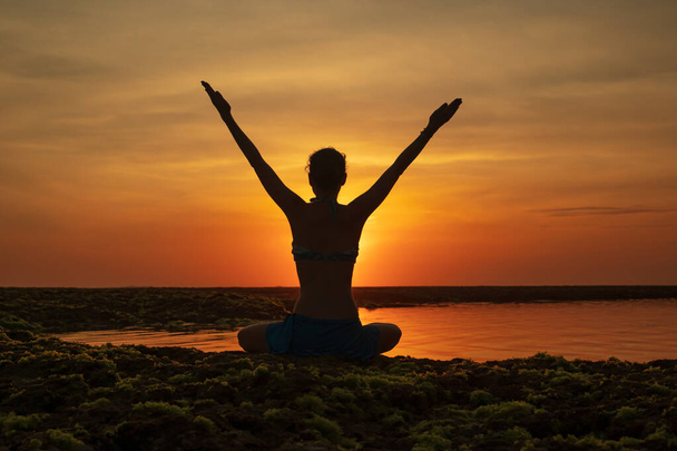 Jovem excitada sentada na praia, levantando os braços em frente ao oceano. Vista de trás. Hora de pôr-do-sol na praia. Bali, Indonésia
. - Foto, Imagem