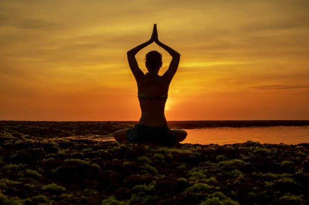 Posizione yoga. Donna seduta sulla spiaggia, che pratica yoga. Giovane donna che alza le braccia con namaste mudra durante il tramonto ora d'oro. Vista da dietro. Spiaggia di Melasti, Bali
.  - Foto, immagini