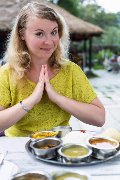 Blonde woman greeting Namaste before the meal in Indian restaurant, dal bhat served - Photo, Image