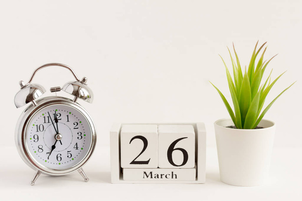 March 26 on a wooden calendar next to an alarm clock and a flower on a white background. The concept of one day a year.Significant date or event - Foto, Bild