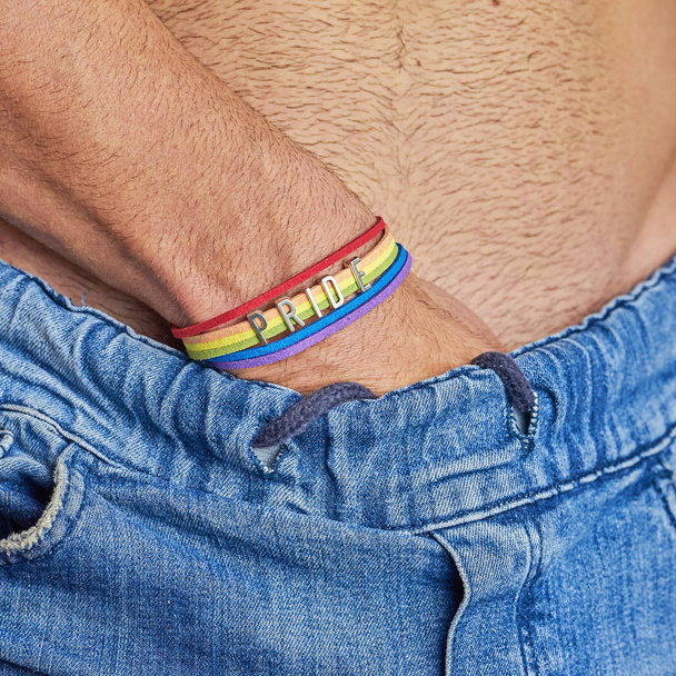 Mannelijke hand met regenboog armband en tekst trots in jeans riem - Foto, afbeelding