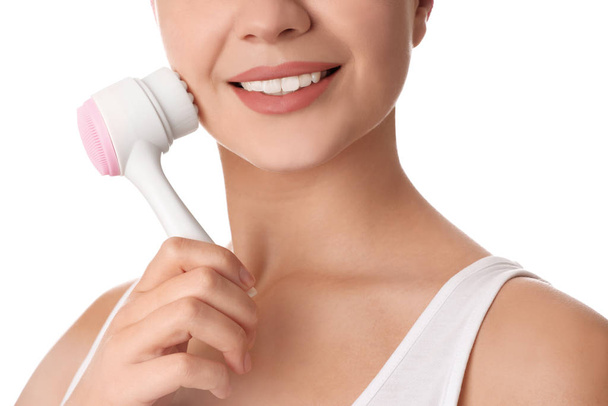 Young woman washing face with cleansing brush on white background, closeup. Cosmetic product - Фото, изображение