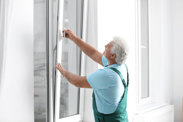 Mature construction worker repairing plastic window indoors - Foto, imagen