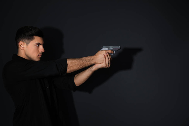 Professional killer with gun on black background - Фото, изображение