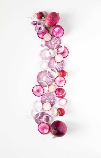 A top down view of a vertical abstract arrangement of overlapping red onion, daikon and radish slices all in a line. - Photo, image