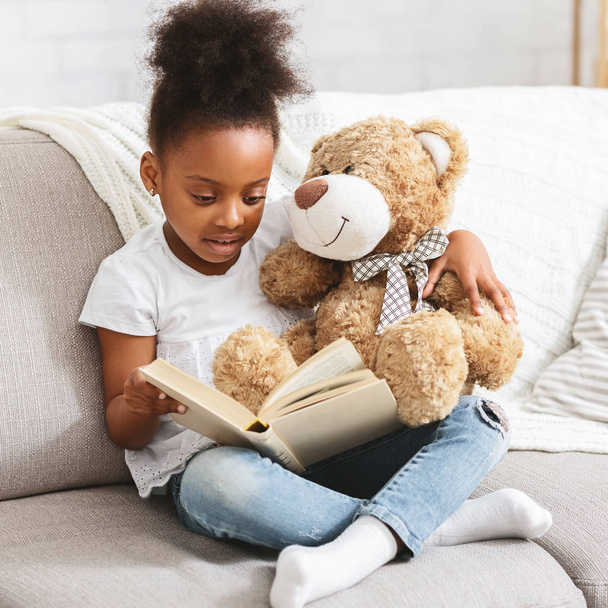 Adorable black kid with teddy bear reading book - Fotoğraf, Görsel