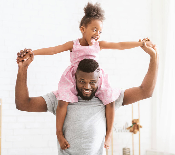 Afrykański tata niesie swoją słodką córeczkę na ramionach - Zdjęcie, obraz