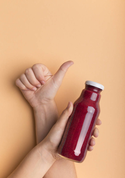 Woman showing thumb up and holding bottle with red beet smoothie - Фото, зображення
