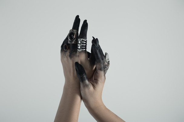 Καλλιεργημένη άποψη του χεριού της μάγισσας σε μαύρο χρώμα με δαχτυλίδια κοσμήματα που απομονώνονται σε γκρι  - Φωτογραφία, εικόνα