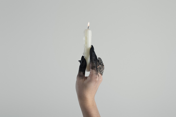 Cropped view of witch hand with jewelry ring and black paint holding candle isolated on grey with copy space - Foto, imagen