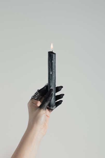 Обрезанный вид ведьмы, держащей свечу в черной раскрашенной руке, изолированный на сером
 - Фото, изображение