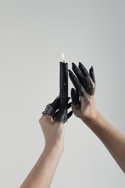 Cropped view of black painted hands of witch with jewelry rings and candle isolated on grey - Foto, immagini