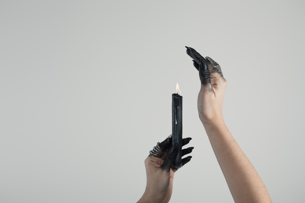 Vágott kilátás boszorkány fekete festett kézzel és ékszer gyűrűk kezében gyertya elszigetelt szürke fénymásolási hely - Fotó, kép