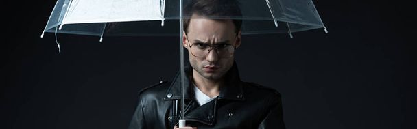 angry stylish brutal man in biker jacket with umbrella isolated on black, panoramic shot - Photo, Image