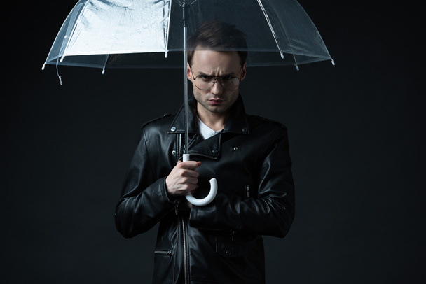 enojado hombre brutal con estilo en chaqueta de motociclista con paraguas aislado en negro
 - Foto, Imagen