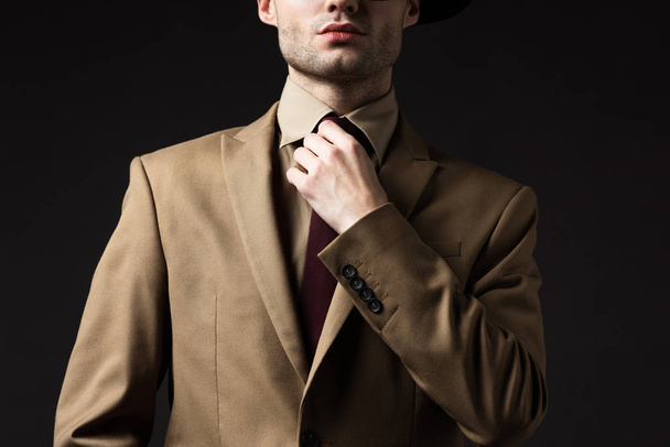 cropped view of elegant man in beige suit fixing tie isolated on black - Fotografie, Obrázek