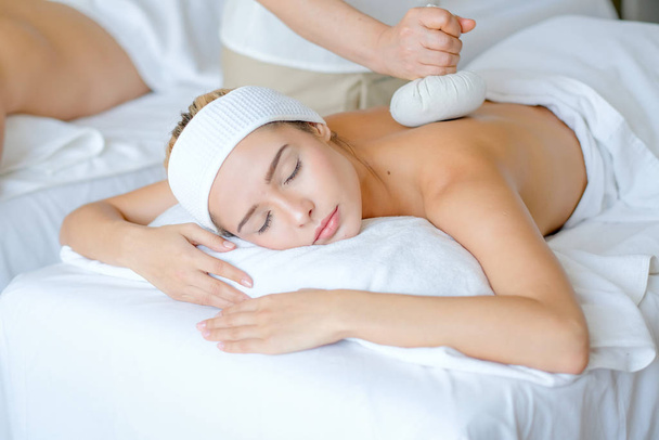 Young beautiful girl enjoy with massage by herbal ball on her back in spa room with day light. - Foto, Bild