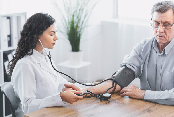 Médico feminino verificando a pressão arterial de homem maduro
 - Foto, Imagem