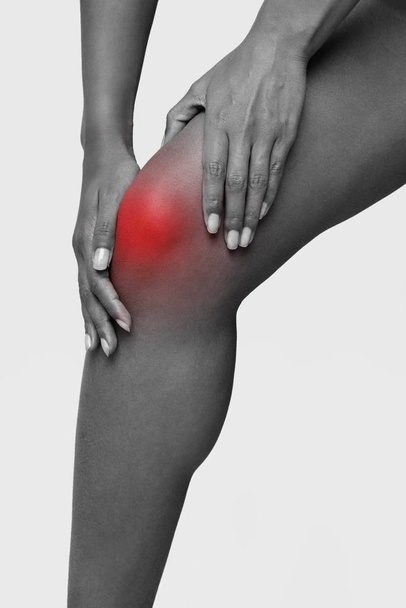 Монохромная обрезанная фотография афро-женщины, массирующей травму колена
 - Фото, изображение