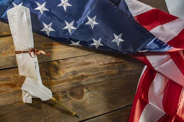 Bandera de EE.UU. y manuscrito antiguo. Documento constitucional enrollado sobre la bandera nacional de América, fondo de madera. Declaración de la Independencia de los Estados Unidos y bandera nacional
 - Foto, imagen
