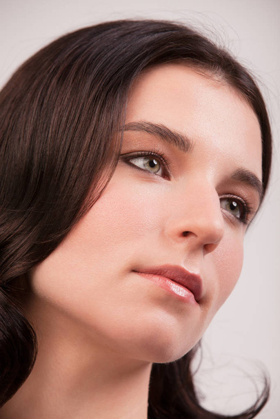Close up face of a young woman with clean fresh skin and dark hair. Young woman looks away from the camera - Foto, immagini