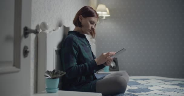 Young female brunette adult working on tablet computer sitting on the bed. Woman making picture of documents by gadget.  - Video