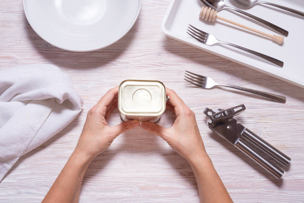 Woman hands opening tin can with corned beef, top view kitchen table - 写真・画像