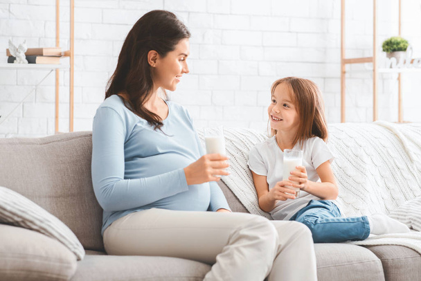 Беременная любящая мама пьет молоко со своей милой дочерью
 - Фото, изображение