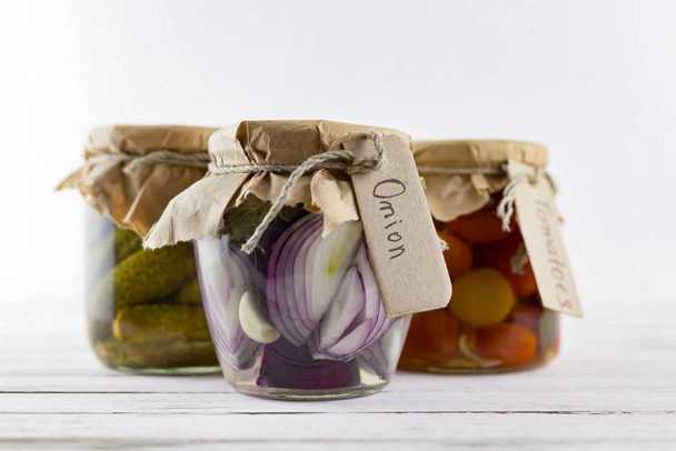 glass jars of fermented white cabbage, cucumbers, tomato, onions. vegetables on a light background. fermentation is a source of probiotic - Photo, Image